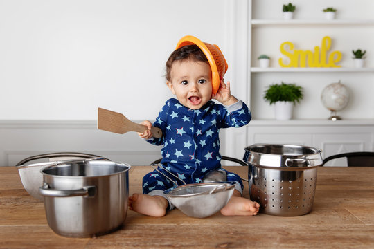 Happy baby playing drums with utensils on kitchen table