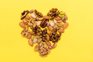 Flat lay ketogenic diet. Walnut,pistachios,pecan,almond are   laid out in the form of heart on the yellow background. Concept of healthy food.