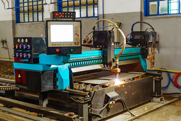Metallurgical laser machine works to cutting metal indoor in the factory. Industrial equipment for cutting metal in process with sparkling light.