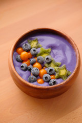 Smoothies of violet color from banana and currant, on top of a blackberry, physalis and kiwi berry. Smoothies in a wooden bowl.