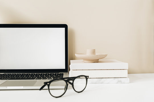 Blank screen laptop. Home office desk table workspace with glasses, notebook on beige background. Copy space mockup blog, website template. Blogger, outsourcing freelancer hero header.