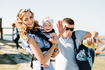 Carrying a baby. Young mother with her daughter in sling. Portrait of happy family. Mom, dad and...
