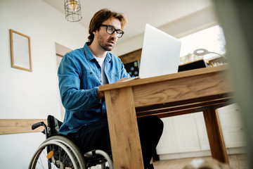 Below view of entrepreneur in wheelchair using laptop while working at home.