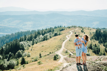Fototapeta premium Portrait of happy family. Mom, dad hugging daughter at nature. Young couple spending time together on vacation, outdoors. The concept of summer holiday. Mother's, father's, baby's day.