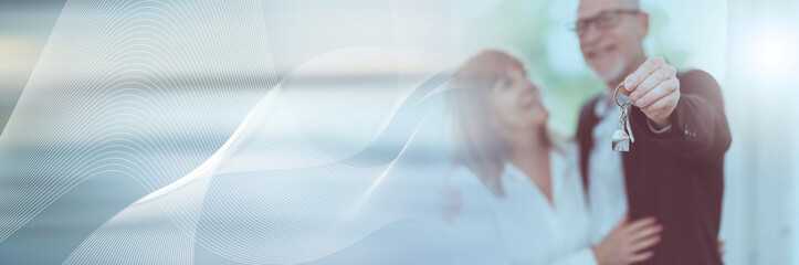 Senior couple showing house keys; panoramic banner