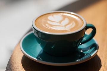 Breakfast in the cafe. Beautiful blue mug with cappuccino or latte coffee on a wooden table. View from above. 