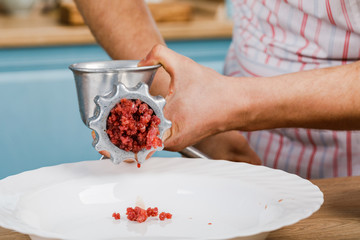 Raw meat. The process of preparing minced meat is carried out using a meat grinder. A male chef uses a meat grinder in the kitchen.