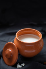 Brown pot with sour cream and a wooden spoon with raisins on a dark background.