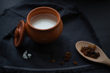 Brown pot with sour cream and a wooden spoon with raisins on a dark background.