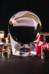 Crystal ball with jars of dried herbs and tincture isolated on black