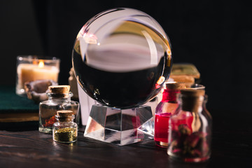 Selective focus of crystal ball with jars of dried herbs and tincture on black background