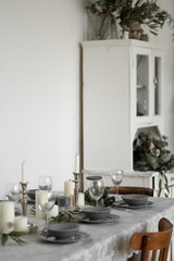 Table setting: gray dishes, white candles, candlesticks, glass goblets, sprigs of eucalyptus on a wooden table 