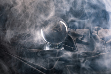 Crystal ball on textile with smoke around on dark background