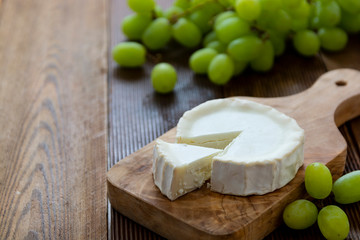 Goat cheeses with grapes, on wooden background isolated. Dark food photo.