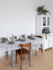 Table setting: gray dishes, white candles, candlesticks, glass goblets, sprigs of eucalyptus on a wooden table 