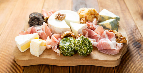Various types of cheeses, grapes, walnuts and honey and prosciutto. Wooden cutting board.