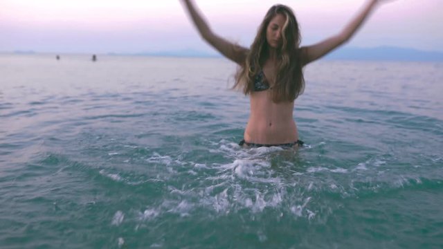 Beautiful slim and young girl swims in the turquoise sea. Long hair and a slender figure in the model. A woman dives under water and splashes. The concept of calm, happiness and relaxation.