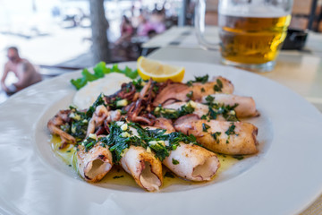 Grilled squids with herbs, garlic and lemon on white plate close-up. Popular and delicious Mediterranean meal.