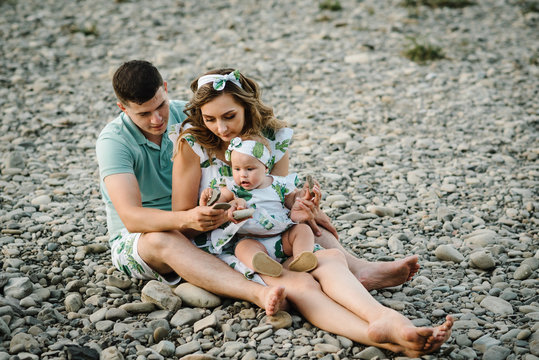 Family playing stones near water. Mom, dad hugging daughter sitting on beach near lake. The concept of summer holiday. Mother's, father's, baby's day. Spending time together. Family look.