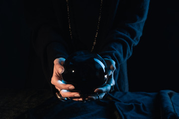 Cropped view of witch with outstretched hands holding crystal ball on black background
