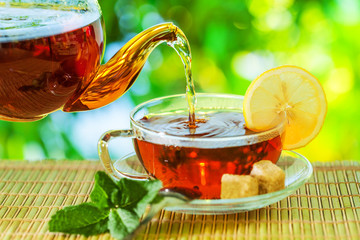 Tea ceremony, pouring tea from a teapot into a tea cup on a background of beautiful nature bokeh.