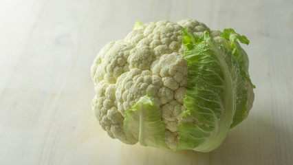 Close-up studio shot of a freshly harvested cauliflower cabbage with green leaves that surround it with hoarfrost water droplets