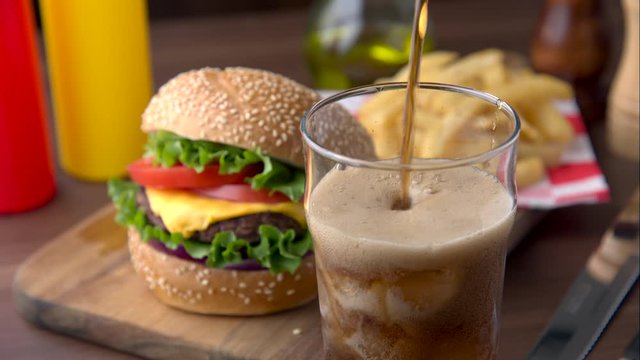 pouring cola into glass with chees burger background
