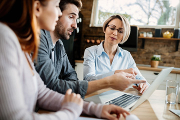 Insurance agent and young couple using laptop during the meeting.