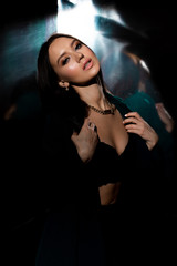 Studio photo of pretty brunette woman in twilight in bra posing to camera. Glossy background
