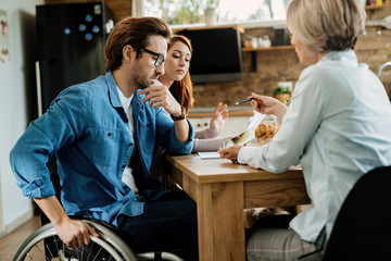 Young disabled man and his wife having a meeting with financial agent at home.