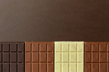 sweets, confectionery and food concept - milk, dark and white chocolate bars on brown background