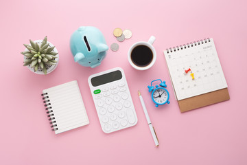 Calculator, piggy bank, calendar, clock and coin on pink desk, flat lay