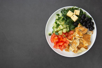 Healthy breakfast. Omelette with fresh mixed vegetables salad rocket, tomatoes, cucumber, olives, cheese. Dark background with copy space. Top view.