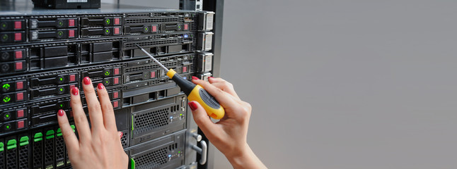 Young woman engineer It with a screwdriver between the server racks in the data center