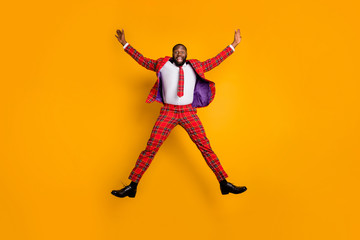 Fototapeta na wymiar Full body photo of crazy funny dark skin guy jump high spend free time rejoicing spread hands wear plaid red costume blazer pants shoes isolated bright yellow color background