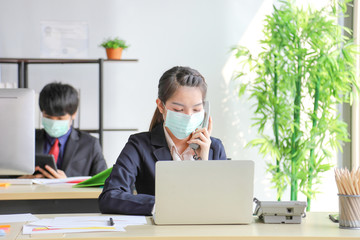 Business workers wearing medical face mask for virus prevention in the office while answering phone...