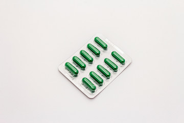 Pharmaceutical tablets, green capsules in blister pack isolated on white background