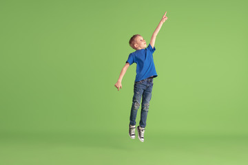 Pointing. Happy boy playing and having fun on green studio background. Caucasian kid in bright...