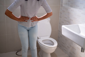 Woman stood in the bathroom in the toilet. With severe diarrhea Use both hands to hold on the stomach, pain, twisting, torture
