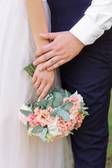 The groom holds the hand of the bride. She has in her hand a tender light wedding bouquet.
