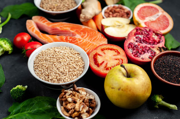 Selection of healthy food: salmon, fruits, seeds, cereals, superfoods, vegetables, leafy vegetables, eggs, rye bread on a stone background