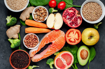 Selection of healthy food: salmon, fruits, seeds, cereals, superfoods, vegetables, leafy vegetables, eggs, rye bread on a stone background