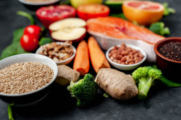 Selection of healthy food: salmon, fruits, seeds, cereals, superfoods, vegetables, leafy vegetables, eggs, rye bread on a stone background