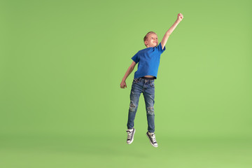 Superhero. Happy boy playing and having fun on green studio background. Caucasian kid in bright...