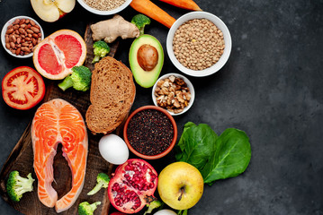 Selection of healthy food: salmon, fruits, seeds, cereals, superfoods, vegetables, leafy vegetables on a stone background   with copy space for your text.Healthy food for people 