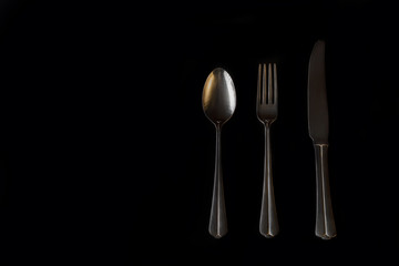 Minimalism on a black background. Three golden table cutlery. Abstraction and creativity.