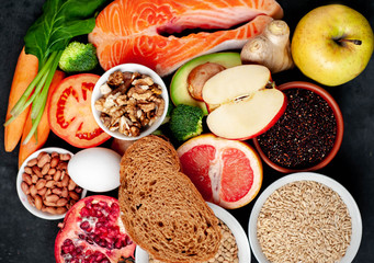 Selection of healthy food: salmon, fruits, seeds, cereals, superfoods, vegetables, leafy vegetables, eggs, rye bread on a stone background