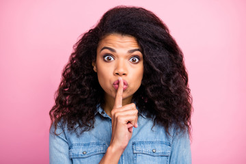 Fototapeta premium Funny funky afro american girl hear unbelievable information impressed say dont share put index finger mouth lips wear denim jeans shirt isolated over pink color background