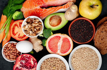 Selection of healthy food: salmon, fruits, seeds, cereals, superfoods, vegetables, leafy vegetables, eggs, rye bread on a stone background