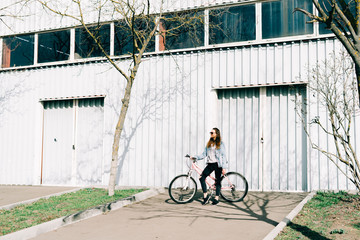 a young stylish girl holds a pink Bicycle standing next to her, against the background of a light...